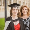 A young woman in graduation garb smiles next to an older woman in UQ's Great Court.